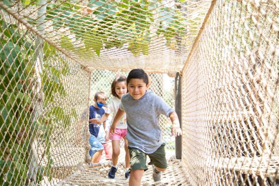 Kids running through The Treehouse's rope tunnel above the exhibits below.