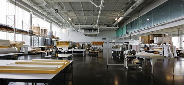 The Serta R&D facility is a double-height space for the study of new and existing products. Raw materials for mattresses, such as springs, padding, and fabric, are stacked on shelves on the south wall, and machinery to construct and run tests on mattresses takes up most of the open floor. The main showroom on the second floor overlooks the work area so that visitors trying out and buying mattresses upstairs can see the product development process.