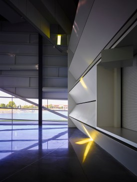 Performance Hall looking west with acoustical sound trap wall on right.  The polished concrete floor connects the inside to the river outside.  One gold glass “note” is visible.  “Notes” appear, move, change and disappear during the day capturing the kinetic energy within the space.