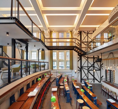 The Auditorium Bar maintains the space's original row desks, while a new steel structure creates a mezzanine-level seating area in the double-height space.
