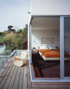 The top-floor master bedroom opens onto a rooftop deck. Two floors below, a sheltered outdoor space tunnels through the building, joining its private and public sides.