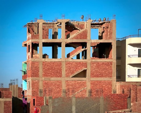 An ashwa’iyyat high-rise in Cairo with yet-to-be completed upper floors. Vertical circulation is expressed on the facade, while voids await the potential customization of infill walls.