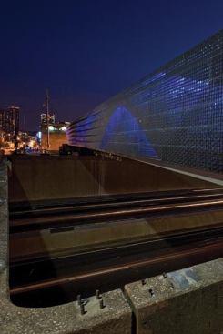 The bridge’s perforated skin illuminates at night and reveals the form of a sine wave.