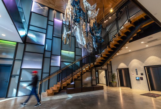 The ground-floor entry to the Moxy Hotel in Columbus, Ohio, features a stair up to the second-floor lobby, anchored by a textile installation from an Ohio artist.
