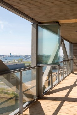 The occupant balconies are inboard of the external trusses and face a waterfront site in Amsterdam's industrial Buiksloterham district.
