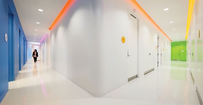 Neutral white light sources illuminate the corridor walls and floor, allowing the fixed-color LED coves to assist with wayfinding.