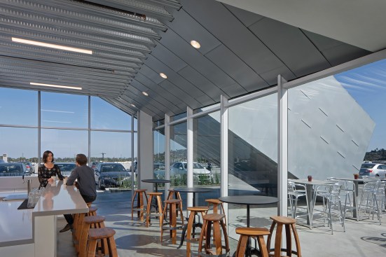 A cafe at the southern end of the building opens onto the garage roof; the sloped metal volume at right is one of two enclosed staircases (one at either end of the new structure) that offer access to the upper office floor.