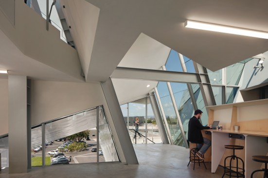 In office interiors, exposed structural steel members frame the irregular geometries of the building volume.