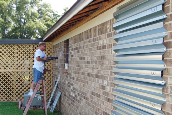 A worker installs corrugated steel shutters over windows of a Florida residence.