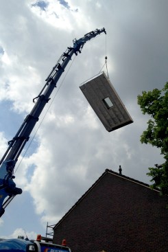 An insulated roof section with integrated structural rails for solar photovoltaic panels is set into place by crane, as part of the Energiesprong retrofits.