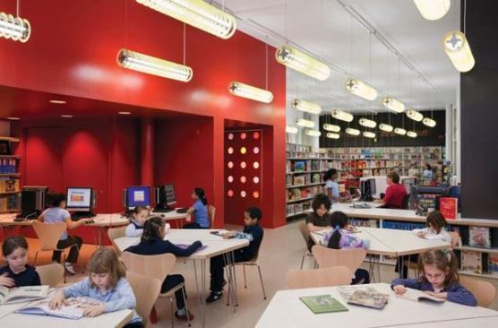 A view of the library at P.S. 31. Custom fixtures were designed with bold color and references the children’s toy Slinkey. The fixture layout and irregular perforated metal louver pattern evoke a kinetic experience.