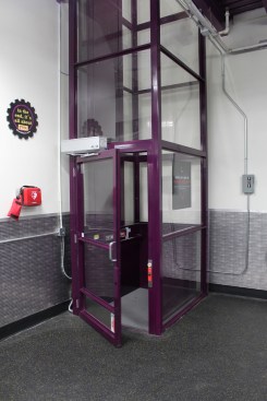 A wheelchair lift in a custom color, like this Savaria V-1504 vertical platform lift installed by Raymond C. Maule and Son in “Planet Fitness Purple,” can emphasize corporate branding and commitment to diversity, equality, and inclusion.