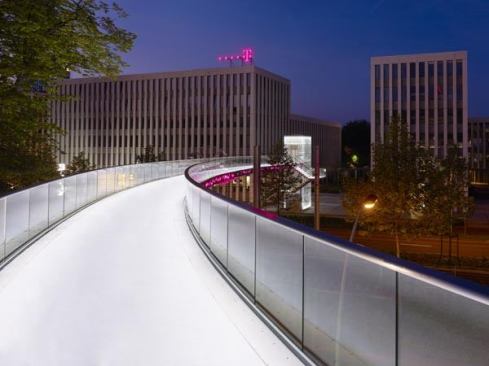 The brightly lit walkway emerges against the nighttime sky and creates an illuminated visual link between the buildings of the Deutsche Telekom campus.