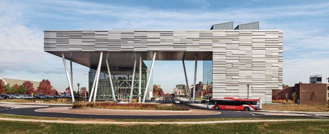 The building’s southwest corner, supported by canted columns, bridges a road onto the campus. Three-dimensional metal panels from Metalwërks clad the west and south façades.