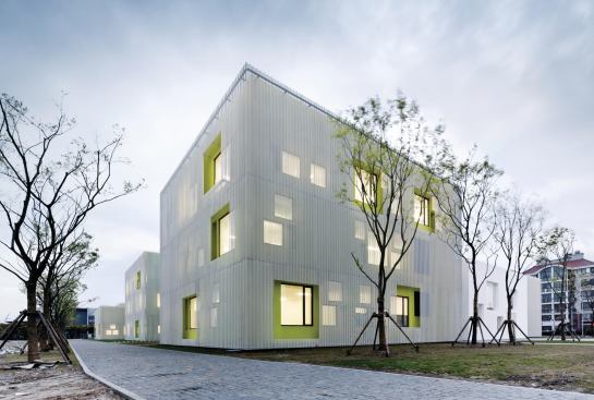 The perforated-metal-screen-clad volumes of the Youth Center are interspersed with white-washed volumes, which the architects used, in combination with the gray brick pavers, to nod back to the traditional building typologies of the region. The windows not only admit daylight, but also help express the interior spaces and program on 

the minimalist façade. 
