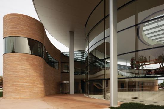 Foster Partners effectively designed two buildings in one, each having its own name and material properties: the glassy Fortaleza Hall and the predominantly masonry Commons. Together, they add 60,000 square feet of employee-focused space to the campus. Fortaleza Hall's minimal form consists of an elliptical glazed shell and overhanging roof. The structure is supported by 10 steel columns, made from custom-designed hollow steel sections. Inside each column is a downspout, allowing rainwater that collects on the roof to run off without requiring the clutter of an exposed gutter system. And despite conventional wisdom that would dictate putting as much glass as possible between inside and out (the average January low temperature in Racine is 13 degrees), each of the 85 curved panes is single-glazed laminated glass. "We were very keen to avoid distortion in the glass, which you get with toughened glass," partner-in-charge Giles Robinson says. "It's regular annealed glass, but laminated to deal with any potential failure, and that system introduced onto the framing system produced what we consider the most elegant solution." Each panel is 7-1/2 feet tall and 16 feet wide. The Commons is a much more solid-looking building. Its brick mass—incorporating employee amenities such as eateries, a wellness center, a bank, a concierge, and a company store—curves around to envelop the east side of the glass pavilion. In contrast to Fortaleza Hall's intentional transparency, the Commons is constructed with self-supporting masonry walls made out of Kasota stone from the same quarry that Frank Lloyd Wright used for the copings of his Administration Building. "I think we were very conscious that we didn't want to mimic or ape the Wright building," Robinson adds, "but we did introduce the bull-nose curves on the end of The Commons that have a resonance to [Wright's] architecture."
