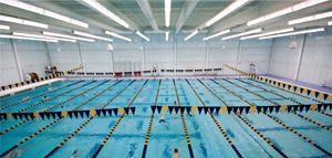 The main feature of the athletic center is the natatorium (above), which houses a competition-regulation swimming pool. The pool is lit with a light-pipe system that uses 1,000W metal halide lamps to provide the required 50-footcandle-level of glare-free illumination on the water surface. Metal halide downlights illuminate the surrounding deck areas.