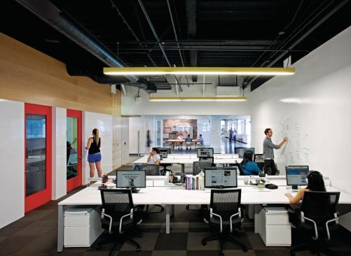 An open-office suite, with conference rooms and enclosed offices lining one wall, and an expansive white board surface on the other.