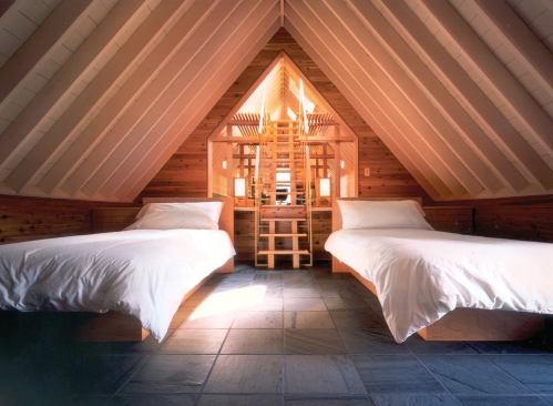 A pair of twin beds in the guest room frames a delicate wooden stair leading to a loft.
