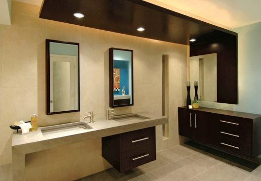 The room’s dark Wenge wood cabinets and backlit canopies provide a stark contrast to the muted beiges and grays of the bath’s slip-resistant porcelain tile and fireslate countertops, sinks, and benches. The fixtures and fittings were chosen for their simp