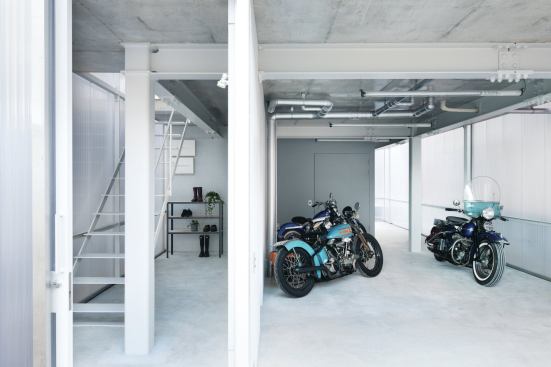 The pocket garage door and sliding front door open the façade at the ground level, revealing the stairway to the main living area and space for up to eight motorcycles.