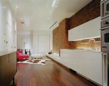 Downstairs, sleek white kitchen cabinetry extends into the living area, where it drops to a low seating shelf with hidden drawers. A drop-down movie screen disappears into the ceiling slot.