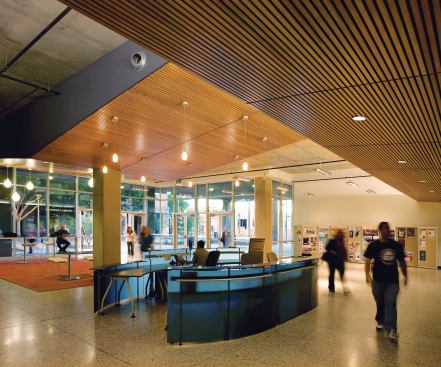 The building's main lobby has café tables and seating for informal meetings, as well as an information kiosk. Unfinished concrete ceilings are softened with a system of wood-clad ceiling soffits that conceal HVAC ducts. STOOLS - Steelcase - Scoop stool - steelcase.com - PENDANT LIGHTING FIXTURES - Louis Poulsen - Moser pendant fixture - louispoulsen.com - DOORS - KT-Fabrication - Exterior aluminum door system - ktfab.com
