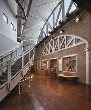 In the white volume, glazing creates light-filled spaces that drive home the contrast between light and dark that exists throughout the space. The dark triangular trusses of the first volume give way to white arced beams, like those in this circulation space by the museum shop.