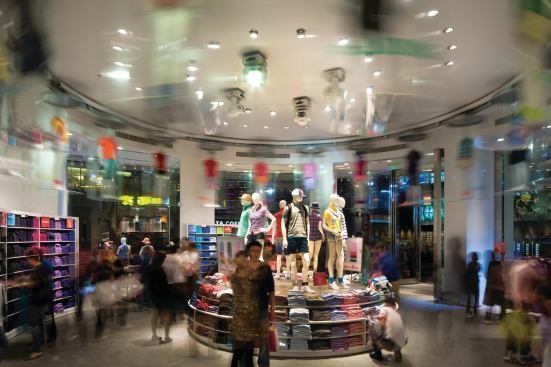 Uniqlo is known for making clothing in a whole spectrum of colors, so the inventory in the store actually becomes part of the design. Here, in the bull-nosed portion of the ground-floor retail space, shoppers are enticed by mannequins in capsules that rotate overhead on a track mounted on the ceiling. Throughout the store, mannequins showcasing the brand's wares are mounted near ceiling height—on ledges ringing the structural columns or on top of shelving—so that customers can see the clothes even from inside a throng of other shoppers.