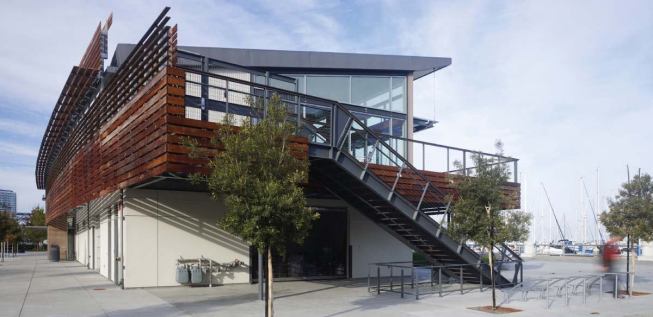 The new Harbormaster's Building is a long, thin structure, located on a series of public docks. Wood continues along the sides of the building to connect the two façades.