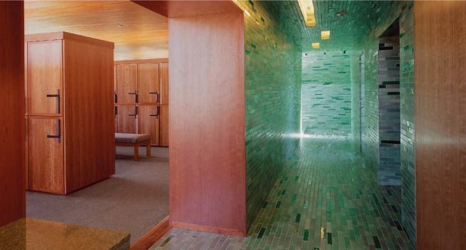Wood gives way to tile in the adjacent wet area, where the floor, walls, and ceiling are clad in handcrafted tile in shades of green that recall water.