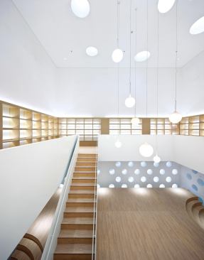 In the library, wood flooring from Armstrong lends warmth to the white double-height space. Circular windows on the lower level look out into one of many courtyards, and terraced seating areas provide gathering spaces for 

the children.