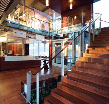 Double-height spaces like this one by the main entrance are used throughout the building to promote interaction between the workers on different floors. Hardwood stair treads are capped with an inset oil-rubbed bronze nosing. Hardwood railings are supported by steel balusters, and 5/8-inch-thick laminated glass completes the handrail assembly.
