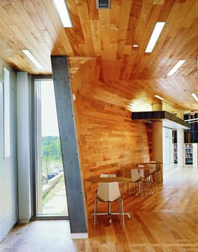 The warmth of the ash planks plays against exposed aluminum and glass fenestration. Careful detailing allows the planks in the ceiling to neatly navigate curves and corners, as seen here in the transition space between the stacks and the casual study area.