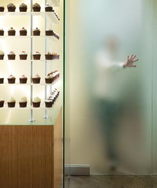 In pursuing the strategy of a bakery that doesn't look like a bakery, one thing the team did not want to sacrifice was the cachet that each cupcake is made on-site. A frosted glass door shielding the kitchen allows customers to see shadows of chefs, smell the baking cake, and hear the whir of the mixers, without seeing spilled flour and messy pastry bags.