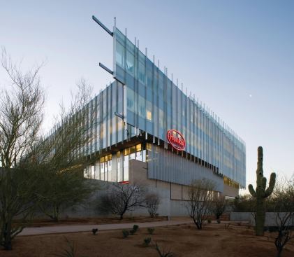 The glass façade extends past the northwest corner of the building, supported by a prefinished aluminum curtain wall system and supports welded to horizontal pipe and tube steel. Mullion caps extend from the top and bottom of the glass surface, creating texture that breaks up the smooth surface.