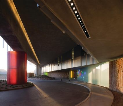 A dip in the façade hidden beneath the monumental glass curtain wall holds a porte-cochere where visitors approach and enter the building out of the sun. Fairly quiet materials such as metal panels, fritted glass, and brick are offset by a brightly colored fiberglass-wrapped column and neon signs that showcase the different consumer brands that fall under the Henkel umbrella.