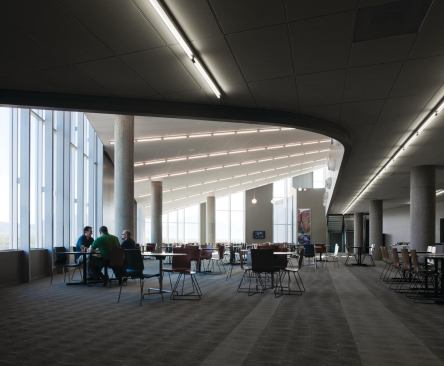 The cafetorium is a mixed-use space in the building, serving as both a staff cafeteria and an auditorium where all of the employees can gather for meetings and events. A canted ceiling plane starts low at the windows and moves higher to accommodate a mezzanine that increases the capacity of the space.
