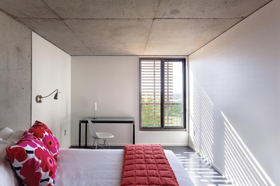Each guest room is a compact 9 feet 9 inches by 19 feet; those dimensions include space for an en-suite bathroom. Floors and ceilings are concrete (covered by resilient flooring and exposed, respectively) with embedded radiant heating and cooling. The movable cypress louver is still visible just outside the window.