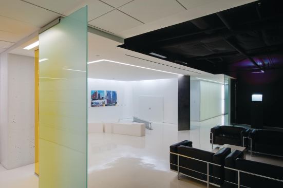 In contrast to the stark whiteness of the rest of the space, the waiting area is coated in black paint and film from 3M, with black leather furniture. This area is set off from the rest of the space by glass panels coated with GlassFilm Enterprises film, which is clear when viewed straight on but appears frosted when viewed from an angle.

Ceiling

3M



Blackout film in matte black

3m.comGlass film

 GlassFilm Enterprises



Lumisty control film on 1/2" glass

glassfilmenterprises.comYellow Glass

McGrory Glass



Color-matched yellow tinted glass

mcgrory-glass.comChair

Cassina



Le Corbusier LC3 lounge chair

cassinausa.com