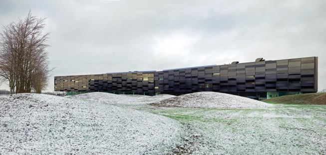 The dark exterior of House of Vestas features adjustable sunscreens made of 3-meter-by-80-centimeter panels of matte and reflective glass. The two-layer system is designed for motion with panels that move in increments of one panel to three panels according to a 3D model.