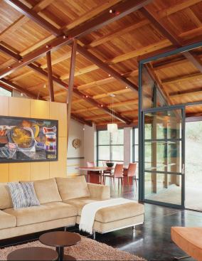 A bank of storage cabinets separates the living area from the kitchen, which is open to the dining room and the broad, sheltering roof above.