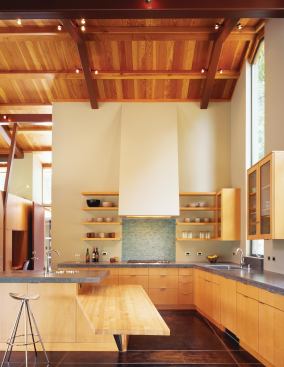 A tall glazing element above the sink frames a view of nearby redwood trees. Its vertical proportions repeat in the plaster-clad range hood and glass-tile backsplash.