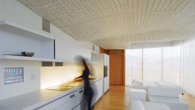 To optimize the house's interior, the team designed a custom ceiling treatment with 4,500 individually formed cells made from window-shade material. The cells both reduce sound reflectivity and pick up natural light at the perimeter, helping to project and diffuse it further into the floor plate. Phase-changing materials in the floor store heat from the sun's rays and radiate it out during cold winter nights, an energy savings that can be tracked on the integrated touchscreens. Making the most of the small floor plan is a deployable bed, which can be retracted into the ceiling when not in use.