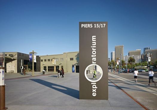 The expanded, punched-out 'O' in the Exploratorium sign turns pedestrians into exhibits in the public plaza outside the new museum space.