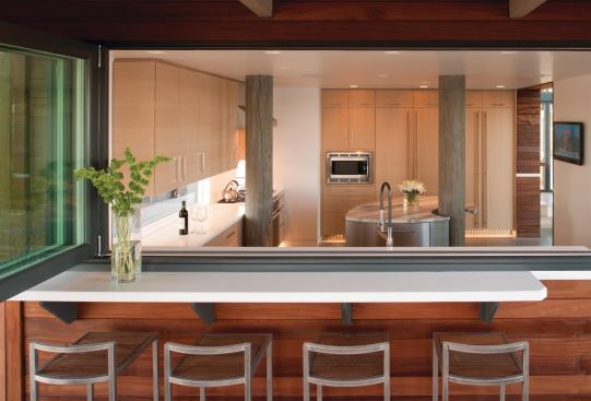 The kitchen's marble-topped island curves around a structural timber. The space contains a pass-through to a covered outdoor dining room.