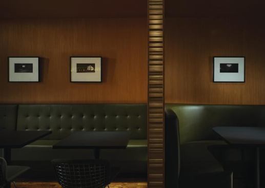 The bench seating on the south wall accommodates four two-person tables. Cherry wood panels are illuminated by concealed light fixtures behind the mossy-green leather seat back. Completing the minimal but rich materials palette for the area is the black honed granite that serves as the table tops — the same material that forms the bar top across the room.