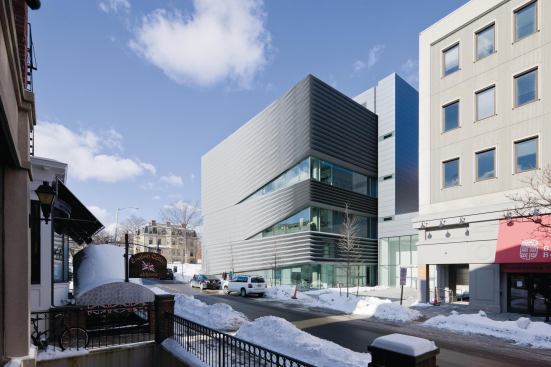 The V-grooved pleats appear like gathered fabric as the panels narrow to reveal bands of glazing that expose the back-of-house spaces. An elevator core is placed outside the main floor plate and wraps up the east façade and up onto the roof plane.