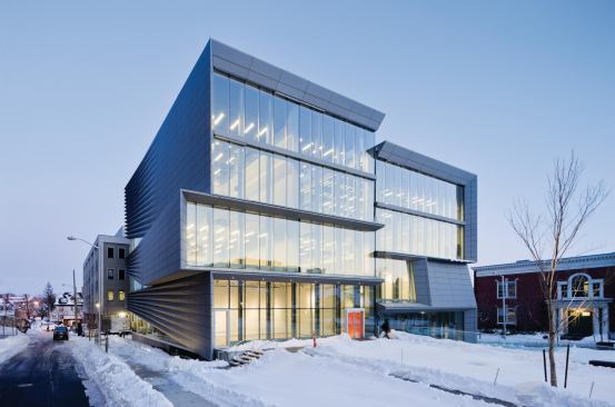 The building is clad in a combination of glazing and CNC-milled zinc composite panels, which start flush against the building where they frame the glazed front façade, and then transition into three-dimensional pleats as they move back toward the rear.
