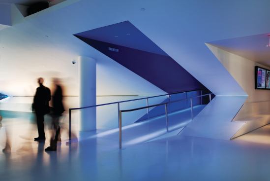 To entice visitors from the sleek white lobby and into the museum's new main 267-seat theater, architect Thomas Leeser created a blue-light-lined ramp entry sequence that hints at the deep blue tones of the space beyond. The rest of the lobby is filled with reception and café areas.